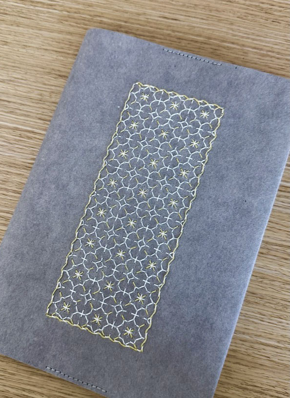 Gold and white stitched panel on a grey notebook cover